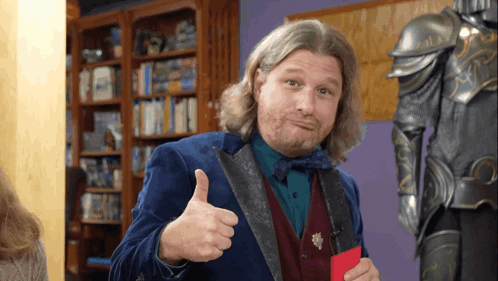 A Man Giving A Thumbs Up In Front Of A Bookshelf GIF