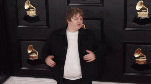 A Man Giving A Thumbs Up In Front Of A Wall With Grammophone Trophies GIF