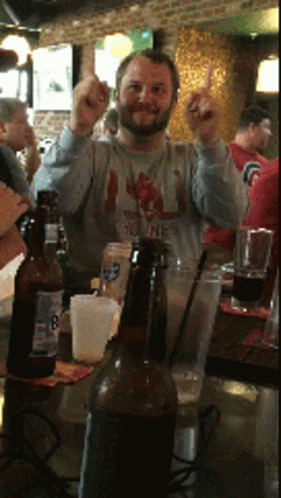 A Man Giving The Middle Finger While Sitting At A Table With Beer Bottles GIF