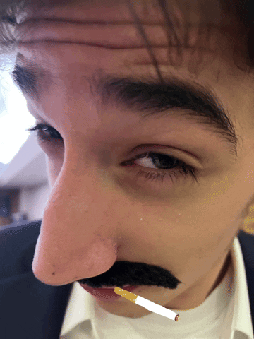 A Man Has A Fake Mustache And A Cigarette In His Mouth GIF