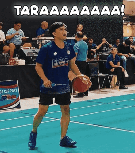 A Man Holding A Basketball And A Badminton Racket On A Court With The Words Taraaaaaaa Written Above Him GIF