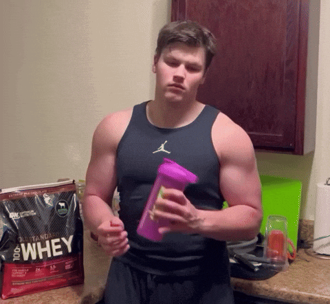 A Man Holding A Bottle In Front Of A Bag That Says 100 % Whey GIF