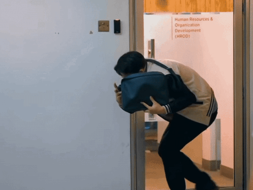 A Man Holding A Briefcase Stands In Front Of A Glass Door That Says Human Resources & Organization Development GIF