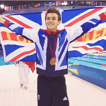 A Man Holding A British Flag With His Arms Outstretched And A Medal Around His Neck GIF
