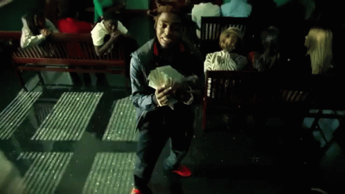 A Man Holding A Bunch Of Money In Front Of A Group Of People Sitting On Benches GIF