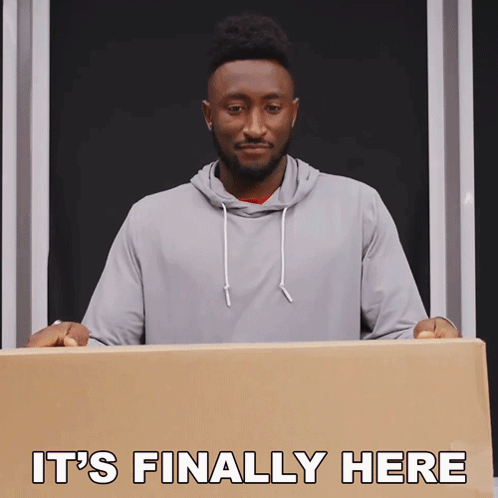 A Man Holding A Cardboard Box With The Words " It 'S Finally Here " Above Him GIF