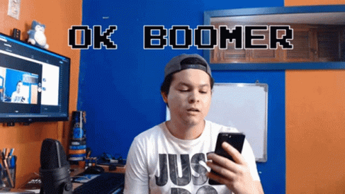 A Man Holding A Cell Phone In Front Of A Sign That Says " Ok Boomer " GIF