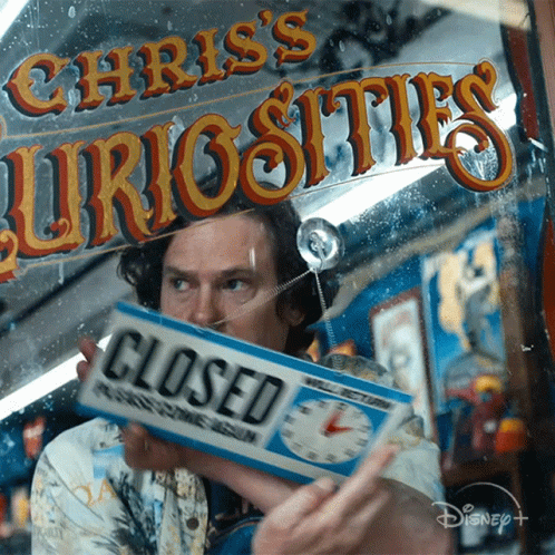 A Man Holding A Closed Sign In Front Of Chris 'S Curiosities Sign GIF