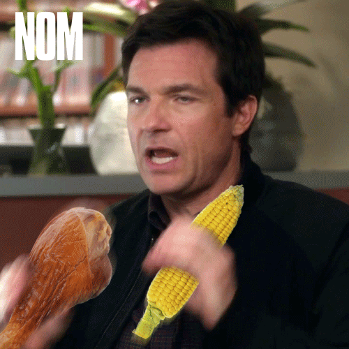 A Man Holding A Corn On The Cob And A Chicken Leg With The Word Nom On The Bottom Right GIF