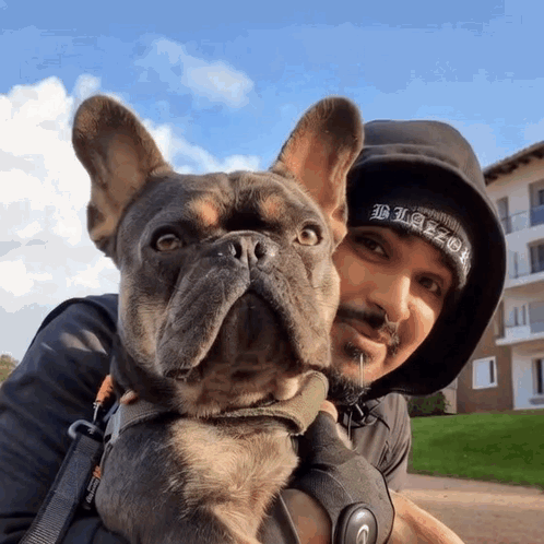 A Man Holding A Dog Wearing A Black Beanie That Says Blaze GIF