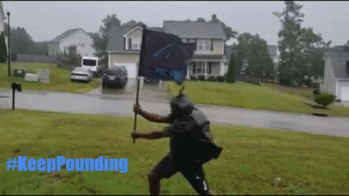 A Man Holding A Flag In The Rain With #Keeppounding Written In Blue GIF