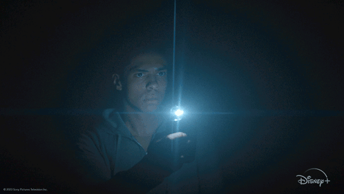A Man Holding A Flashlight In A Dark Room With A Disney + Logo GIF