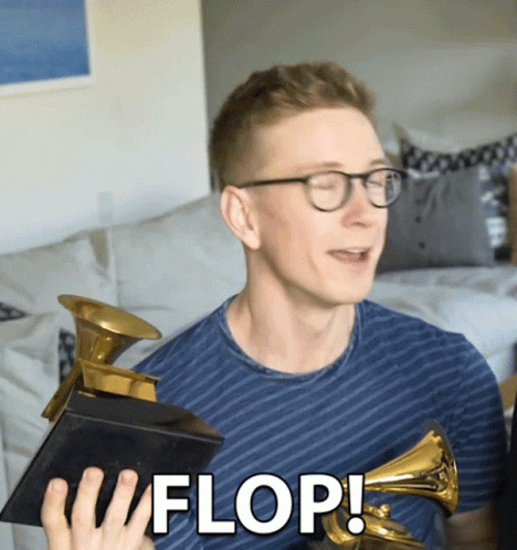 A Man Holding A Grammy Trophy With The Word Flop Written On It GIF