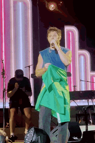 A Man Holding A Green And Yellow Flag On Stage GIF