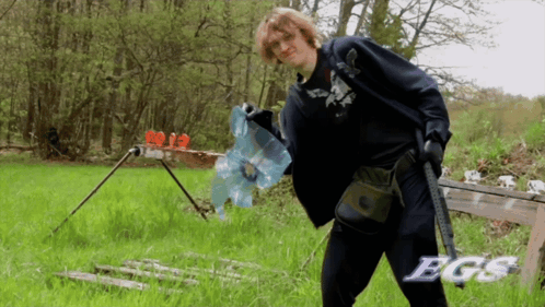 A Man Holding A Gun In A Field With The Word Bgs On The Bottom Right GIF