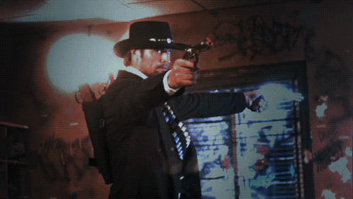 A Man Holding A Gun In Front Of A Window With Graffiti On It GIF