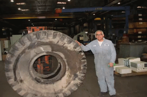 A Man Holding A Large Tire In A Warehouse With A Crane In The Background That Says Lsb GIF