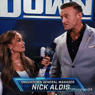 A Man Holding A Microphone Next To A Woman With The Name Nick Aldis GIF