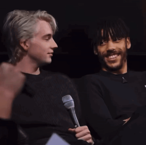 A Man Holding A Microphone Next To Another Man Who Is Smiling GIF