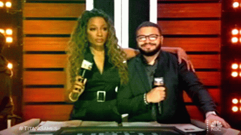 A Man Holding A Microphone Stands Next To A Woman Who Is Holding A Microphone And The Words Titan Games Are On The Scree GIF