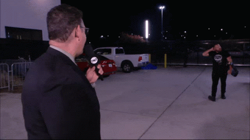 A Man Holding A Microphone That Says Tnt Stands In A Parking Lot GIF