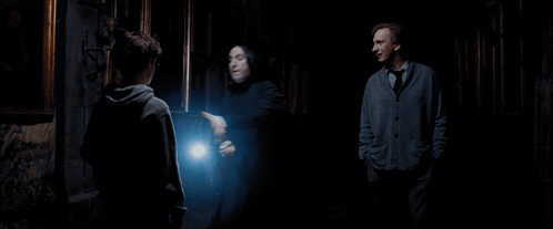 A Man Holding A Piece Of Paper Is Surrounded By Two Other Men In A Dark Room GIF