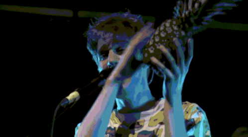 A Man Holding A Pineapple In Front Of His Face While Singing Into A Microphone GIF