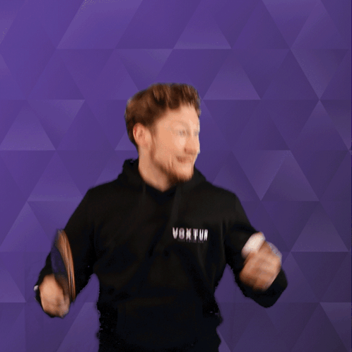 A Man Holding A Ping Pong Paddle And Wearing A Black Hoodie That Says Voxtui GIF