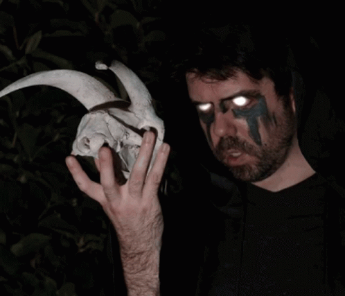 A Man Holding A Skull With Horns And Glowing Eyes GIF