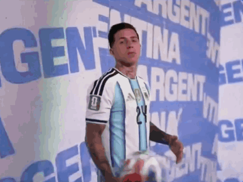 A Man Holding A Soccer Ball In Front Of A Sign That Says Argentina GIF