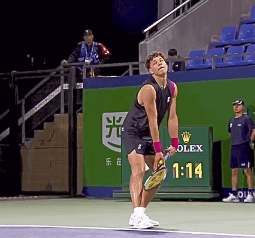 A Man Holding A Tennis Racquet On A Tennis Court With A Rolex Sign Behind Him GIF