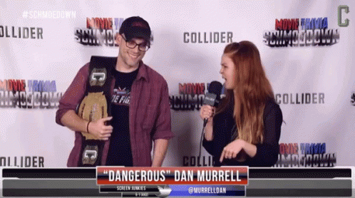 A Man Holding A Wrestling Belt Talks To A Woman In Front Of A Screen That Says " Dangerous " Dan Murrell GIF