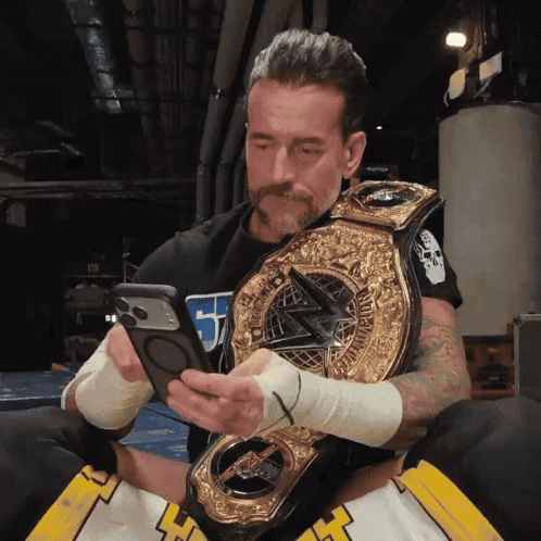 A Man Holding A Wrestling Championship Belt Looking At His Phone GIF