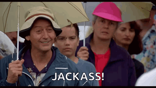 A Man Holding An Umbrella Says Jackass In A Crowd GIF