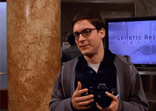 A Man Holds A Camera In Front Of A Screen That Says Genetic Research GIF