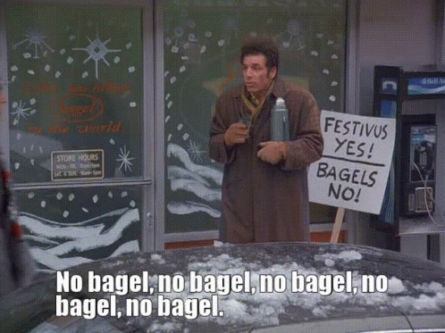 A Man Holds A Sign That Says Festivus Yes Bagels No GIF