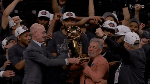 A Man Holds A Trophy In Front Of A Group Of Basketball Players GIF