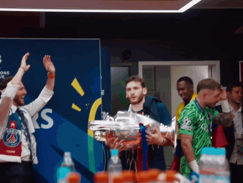 A Man Holds A Trophy In Front Of A Wall That Says Champions League GIF