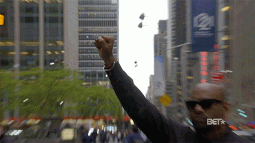 A Man Holds His Fist Up In The Air In Front Of A Sign That Says Bet GIF