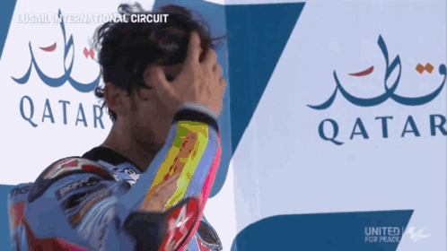A Man Holds His Head In Front Of A Qatar Logo GIF