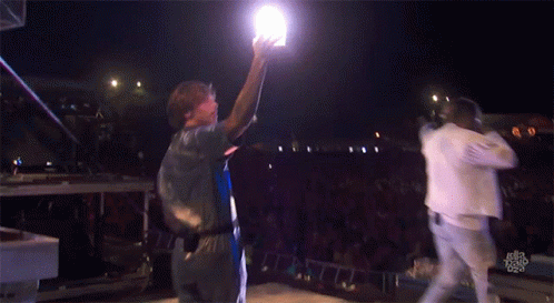 A Man Holds Up A Light While Standing On A Stage GIF