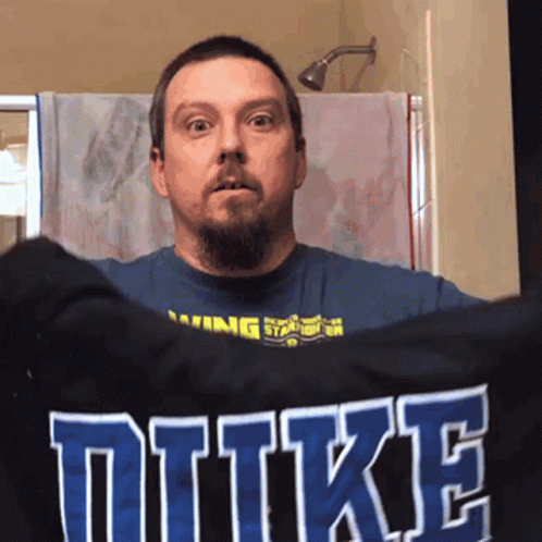 A Man Holds Up A Shirt That Says Duke GIF