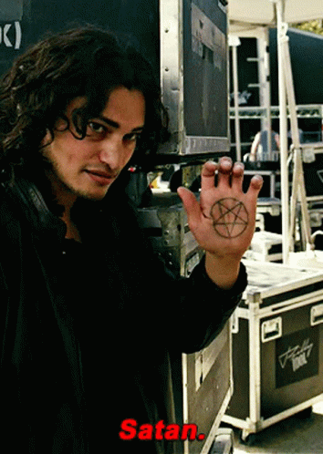 A Man Holds Up His Hand With A Pentagram On It And The Word Satan Written Below Him GIF