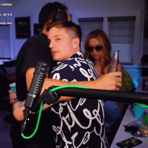 A Man Hugging Another Man In Front Of A Microphone That Says Jcmile On The Bottom Right GIF
