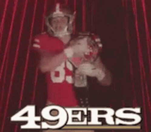 A Man In A 49Ers Jersey Is Standing In Front Of A Red Curtain GIF