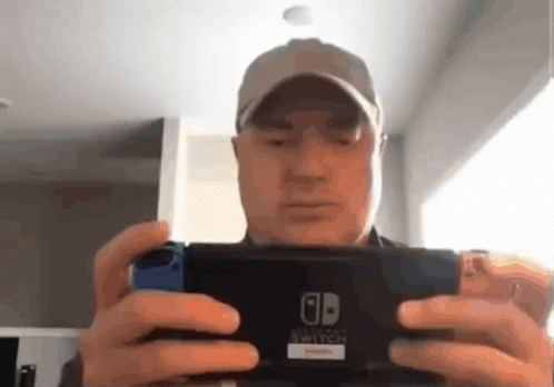 A Man In A Baseball Cap Is Holding A Nintendo Switch In His Hands GIF