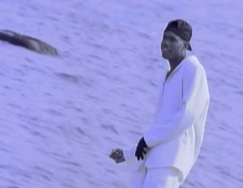 A Man In A Baseball Cap Is Standing In Front Of A Body Of Water GIF