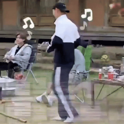 A Man In A Baseball Cap Is Standing In Front Of A Group Of People Sitting In Chairs And A Table . GIF