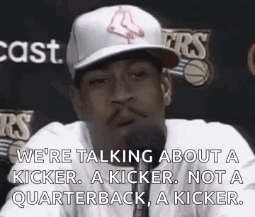 A Man In A Baseball Cap Is Talking Into A Microphone While Wearing A White Shirt . GIF
