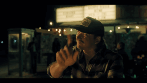 A Man In A Baseball Cap Stands In Front Of A Sign That Says ' Live Free ' GIF